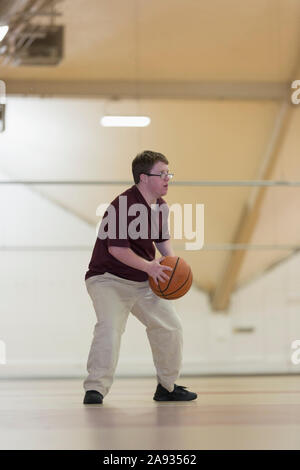 Junger Mann mit Down-Syndrom spielt Basketball in der Schule Turnhalle Stockfoto