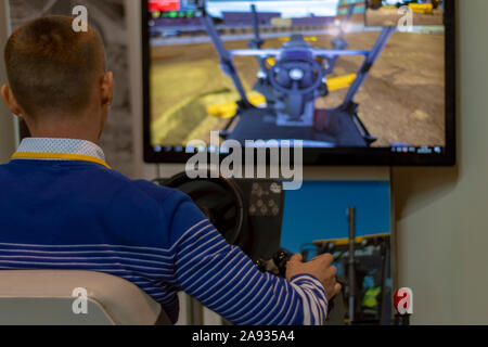 Ein Mann steuert einen Traktor Simulator - ein Bagger, Ansicht von hinten. Bryansk, Rußland - 30. September 2019. Stockfoto