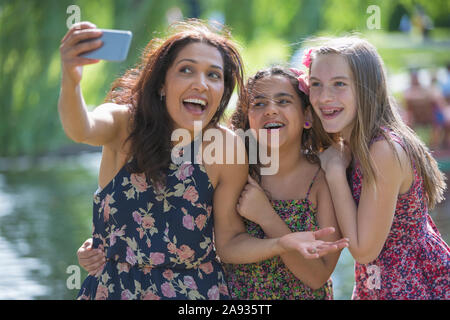Glücklich hispanische Mutter mit zwei teen Töchter mit Zahnspange nehmen Selfie mit Handy im Park Stockfoto