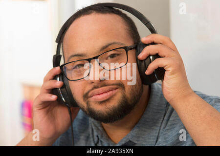 Glücklicher afroamerikanischer Mann mit Down-Syndrom, der Musik hört Mit Kopfhörern zu Hause Stockfoto