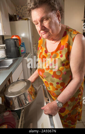 Blinde ältere Frau, die ihren Geschirrspüler in der Küche benutzt Stockfoto