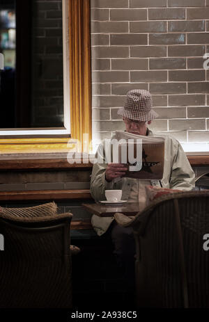 Mann liest Zeitung und Tee trinken im Café zu Barter Books, Alnwick, Northumberland, Großbritannien Stockfoto