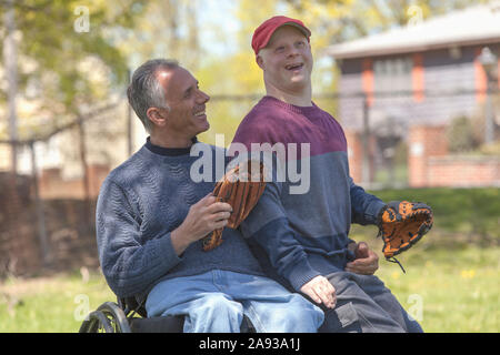 Glücklicher Vater mit Rückenmarksverletzung und sein Sohn mit Down-Syndrom zu spielen Baseball im Park Stockfoto