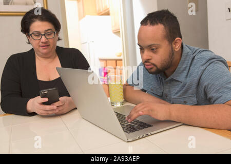 Afroamerikanischer Mann mit Down-Syndrom mit einem Laptop mit Seine Mutter zu Hause Stockfoto