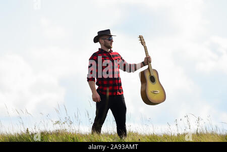 Country Music Konzept. Gitarrist Land Sänger stand im Feld Himmel Hintergrund. Landhausstil. Sommer Urlaub. Wandern Song. Inspiriert land Musiker. Stockfoto