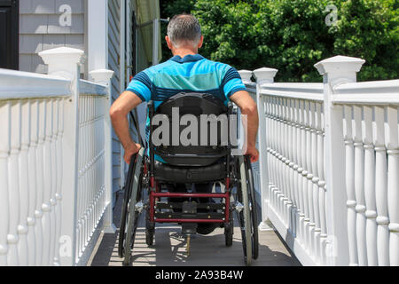 Mann mit einer Rückenmarksverletzung im Rollstuhl beim Betreten des Rampe seines Hauses Stockfoto