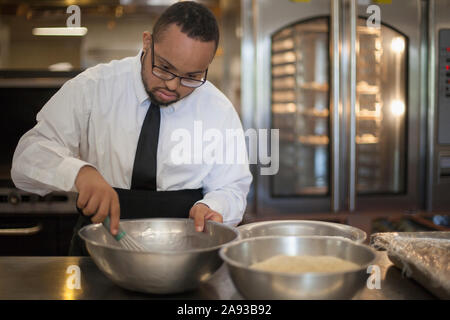 Afroamerikanischer Mann mit Down-Syndrom als Koch Kochen In der kommerziellen Küche Stockfoto