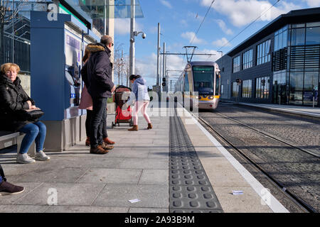 Pendler warten auf eine Plattform wie die LUAS-Straßenbahn in den Vororten von Dublin auf kalten brisk Herbst Tag ankommt Stockfoto