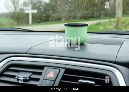 Blick durch die Autoscheibe an einem regnerischen Tag, mit einem grünen Flasche Trinkbecher auf dem Armaturenbrett. Stockfoto