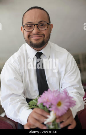 Porträt von glücklichen afroamerikanischen Mann mit Down-Syndrom als Ein Kellner fixiert Blumen in Vase auf dem Tisch Stockfoto