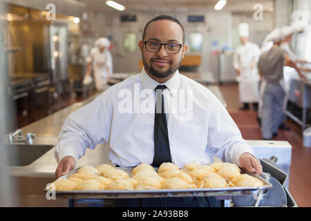 Afroamerikanischer Mann mit Down-Syndrom als Koch hält Ein Tablett mit Cookies in der kommerziellen Küche Stockfoto