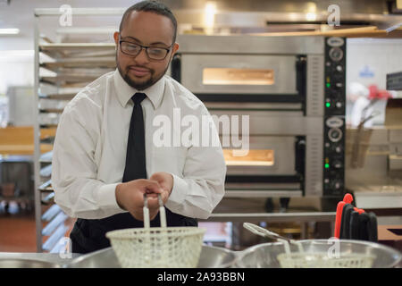 Afroamerikanischer Mann mit Down-Syndrom als Koch Kochen In der kommerziellen Küche Stockfoto