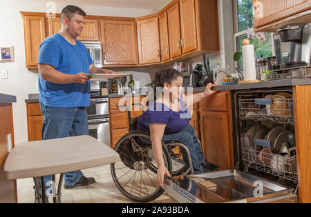 Frau mit Spina Bifida und ihr Mann mit der Spülmaschine In der Küche Stockfoto