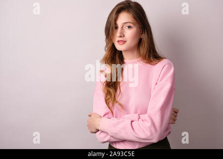 Einem blonden Mädchen in einem rosa sweatshirt auf weißem Hintergrund und schmiegt sich mit ihren Händen steht, sieht in den Rahmen Stockfoto