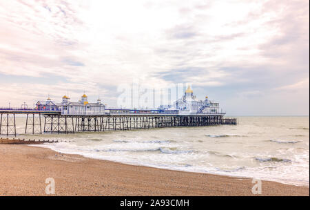 Früh morgens auf einem Kieselstrand in Eastbourne. Ein Strand mit Wellen im Vordergrund steht und ein Pier darüber hinaus. Eine Dämmerung Himmel über. Stockfoto