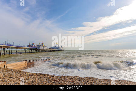 Früh morgens auf einem Kieselstrand in Eastbourne. Eine Welle bricht gegen einen hölzernen Wellenbrecher im Vordergrund und ein Pier ist darüber hinaus. Stockfoto