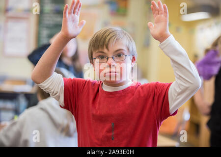 Junge mit Down-Syndrom Arme in einer Schule Klassenzimmer angehoben Stockfoto