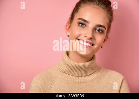 Ein Mädchen mit einem Fernlicht steht in einem Pullover gegen einen rosa Hintergrund und lächelt in den Rahmen. Stockfoto