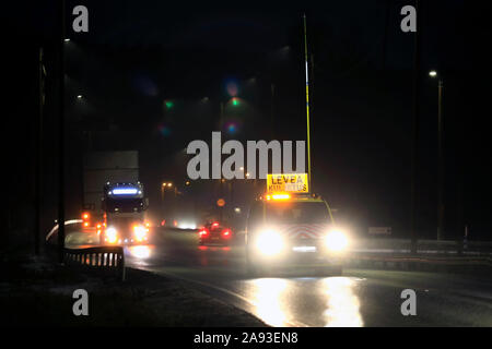 Pilot Fahrzeug vor einem Auflieger für den Transport von übergroßen Last eines 5,5 m hohen Stahlkonstruktion in einer regnerischen Nacht in Salo, Finnland. Nov 8, 2019. Stockfoto