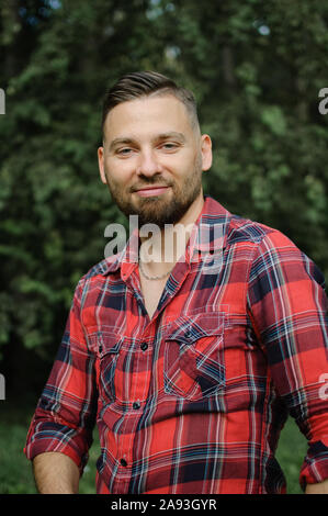 Outdoor Portrait von gutaussehenden jungen Mann mit Bart in den Park entspannt auf grüne Bäume Hintergrund. Hüfthose style Konzept. Stockfoto