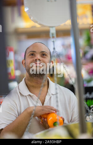 Mann mit Down-Syndrom Wiegen Gemüse in einem Lebensmittelgeschäft Stockfoto