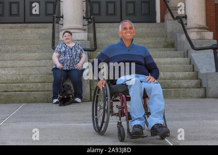 Mann mit Rückenmarksverletzung sitzt im Rollstuhl mit seinem Tochter im Hintergrund, die blind ist Stockfoto