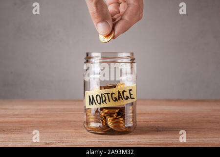 Glas Glas mit Münzen und eine Inschrift Hypothek. Mann hält Münze in der Hand Stockfoto