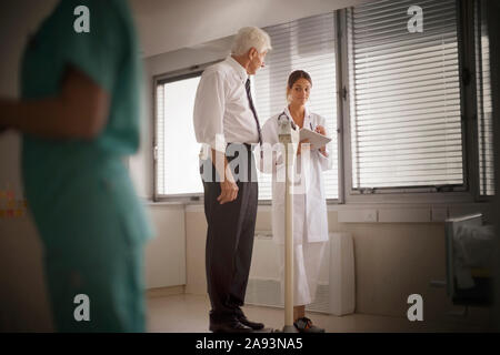 Ansicht eines Arztes, der sein Gewicht auf einem Wiegen überprüft Maschine Stockfoto