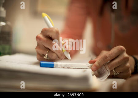 Hände einer Ärztin, die auf einem medizinischen Test schreibt Tube mit einem Stift Stockfoto