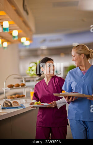 Zwei junge Krankenschwestern lächeln und unterhalten sich miteinander, wenn sie kommen Ihr Mittagessen aus der Kantine des Krankenhauses Stockfoto