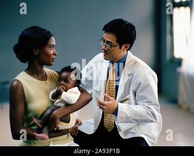 Junge Frau hält ihr kleines Baby, während sie mit ihrem Mann Arzt Stockfoto