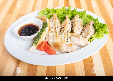 Gyoza auf Platte, mit Kräutern und Sauce. Stockfoto