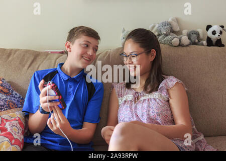 Teenager-Mädchen, die Lernfähigkeit hat Blick auf Telefon mit Ihr Bruder Stockfoto