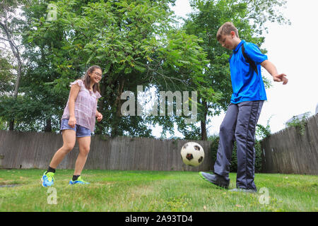 Teen Mädchen, die hat Lernen Behinderung Fußball spielen mit ihr Bruder Stockfoto