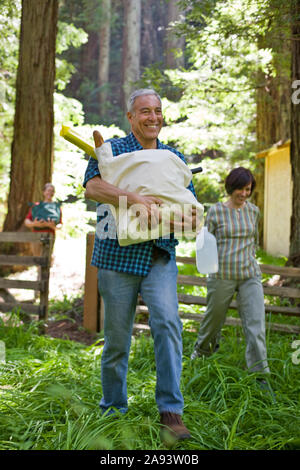 Lächelnd reifer Mann, der einen Beutel mit Nahrung durch einen Wald mit Freunden.. Stockfoto