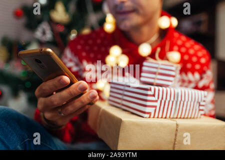 Christmas shopping online. Mann Kaufen Neu Jahr präsentiert sie ihr Smartphone. Guy holding Geschenkboxen und Telefon von Baum Stockfoto