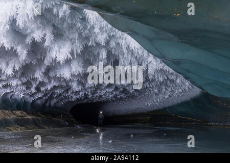 Ein Mann mit Stirnlampe erkundet eine Eishöhle des Castner Glacier mit Raureif an der Decke; Alaska, USA Stockfoto