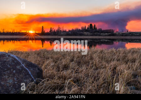 Eine Rauchwolke, die aus dem Feuer der Oregon Lakes von 2019 aufsteigt, reflektiert in einem See bei Sonnenuntergang, südlich von Delta Junction; Alaska, Vereinigte Staaten von Amerika Stockfoto