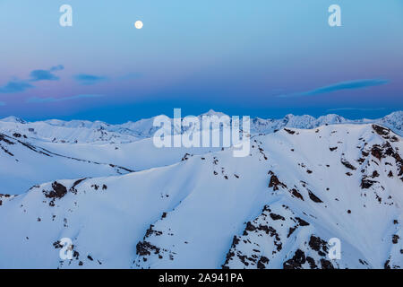 Der Mond steigt über verschneiten Bergrücken nach Sonnenuntergang in der Alaska Range; Alaska, Vereinigte Staaten von Amerika Stockfoto