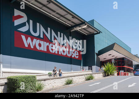 Die Menschen drücken Wagen hinter einem großen Bunnings Warehouse-Logo an der Seite eines Ihrer großen DIY-Verkaufsstellen im Sydney Vorort von belrose. Stockfoto