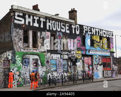 Bauherren vor einem heruntergekommenen Gebäude von hausbesetzern besetzt und in Graffiti protestieren gegen Gentrifizierung abgedeckt. Hackney Wick, East London. Stockfoto