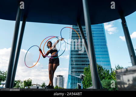 Perspektivische Ansicht der jungen Frau tanzen mit vier Hula Hoop in der Stadt Stockfoto
