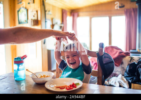 Vater erreichen, um seinen Sohn zu kitzeln, während am Tisch Stockfoto