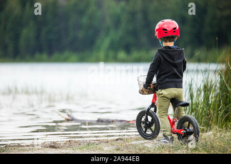 Ansicht der Rückseite des Jungen auf dem Fahrrad mit Blick auf den See. Stockfoto