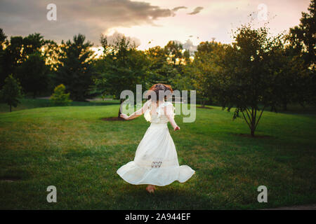 Eine Tänzerin in langen weißen Kleid twirls in goldenem Licht im Park bei Sonnenuntergang Stockfoto