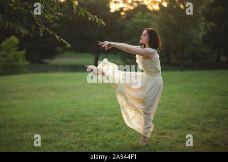 Eine junge Frau tanzt barfuß in einem von Bäumen gesäumten Park bei Sonnenuntergang Stockfoto