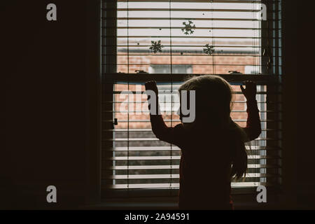 Ein kleines Mädchen steht vor einem Fenster mit Schneeflocke Aufkleber auf. Stockfoto