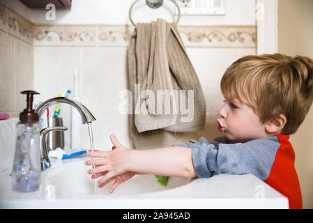 Ein kleiner Junge wäscht seine Hände in das Waschbecken im Bad. Stockfoto