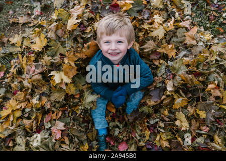 Ein kleiner Junge sitzt in einem Stapel von Blättern. Stockfoto