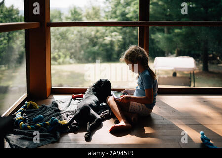 Ein kleines Mädchen sitzt mit ihrem Hund auf einer Veranda. Stockfoto